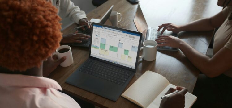 Introducing the New Microsoft Planner (Everything You Need to Know) Three people in a meeting at a table discussing schedule on their Microsoft laptop